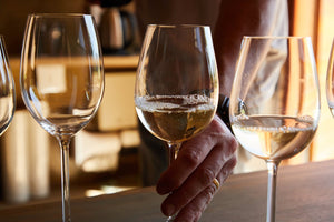 A hand reaches for a glass of white wine during a wine tasting.