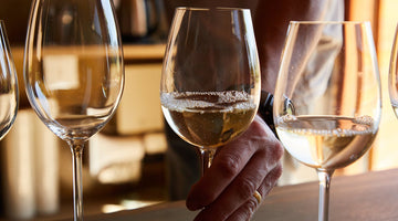 A hand reaches for a glass of white wine during a wine tasting.